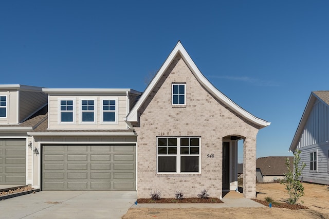 view of front of property featuring a garage, driveway, brick siding, and roof with shingles