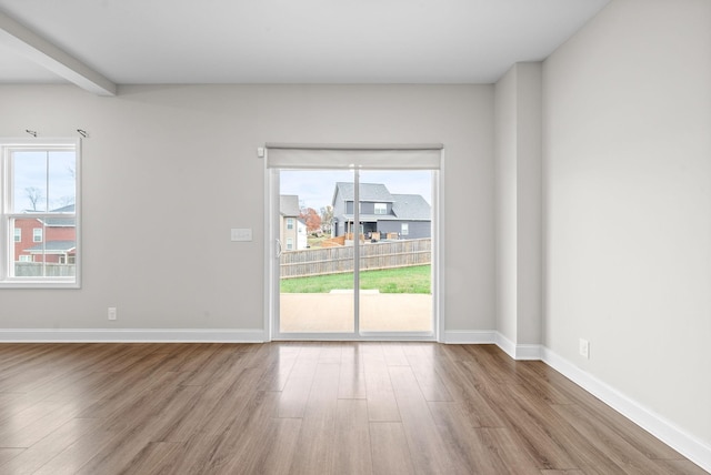 unfurnished room with wood finished floors, beam ceiling, and baseboards