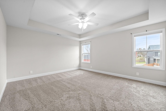 empty room featuring ceiling fan, carpet, a raised ceiling, and baseboards