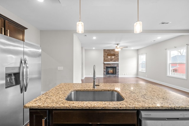 kitchen featuring dark brown cabinetry, stainless steel fridge, dishwashing machine, hanging light fixtures, and a sink