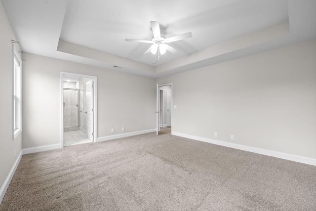 unfurnished room featuring a raised ceiling, light colored carpet, ceiling fan, and baseboards