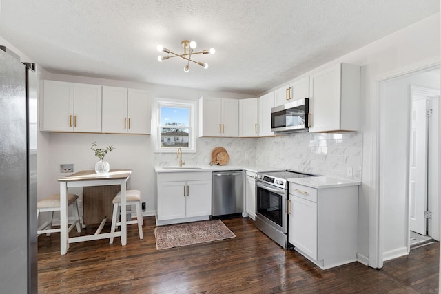 kitchen featuring a sink, light countertops, appliances with stainless steel finishes, backsplash, and dark wood finished floors