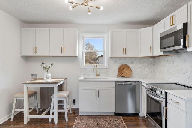 kitchen with dark wood finished floors, decorative backsplash, appliances with stainless steel finishes, light countertops, and a sink