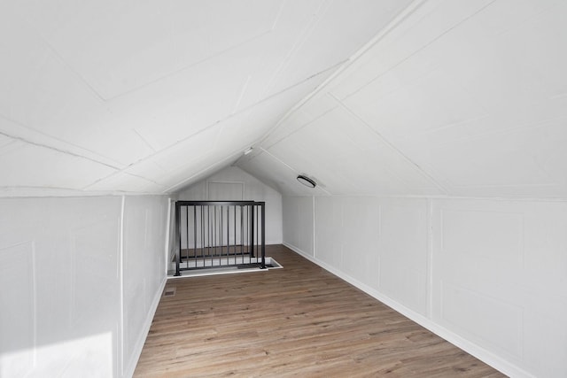 additional living space with lofted ceiling, a decorative wall, and wood finished floors