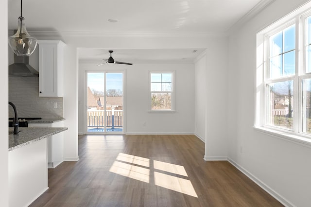 unfurnished dining area featuring a ceiling fan, baseboards, ornamental molding, and dark wood-type flooring