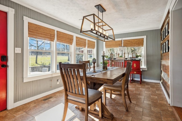 dining area with stone tile floors, ornamental molding, a textured ceiling, a chandelier, and baseboards