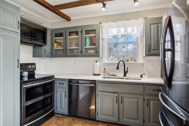 kitchen featuring gray cabinetry, a sink, appliances with stainless steel finishes, tasteful backsplash, and glass insert cabinets