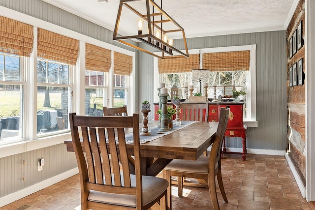 dining area with a notable chandelier, stone tile flooring, ornamental molding, a textured ceiling, and wooden walls