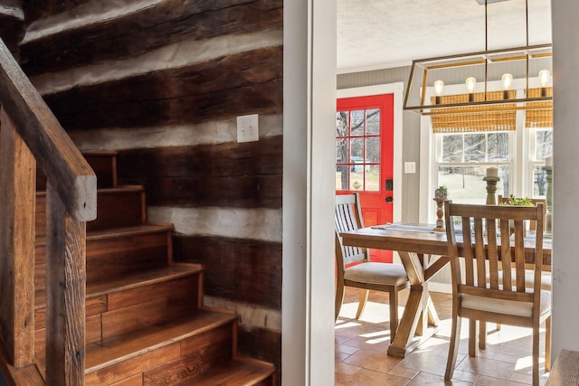 staircase featuring a chandelier, ornamental molding, a textured ceiling, and stone tile floors