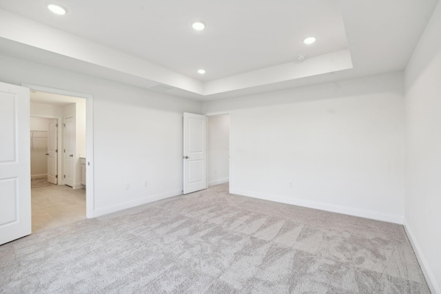 unfurnished bedroom featuring a tray ceiling, light carpet, baseboards, and recessed lighting