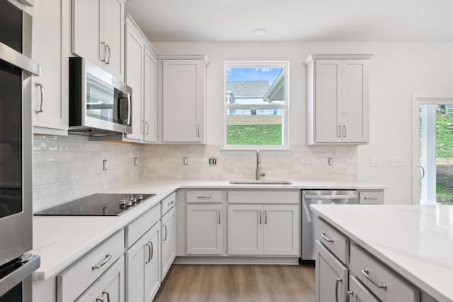 kitchen with light stone counters, light wood finished floors, stainless steel appliances, decorative backsplash, and a sink