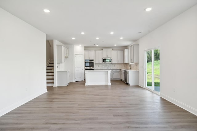 kitchen featuring decorative backsplash, open floor plan, stainless steel appliances, light wood-type flooring, and a sink