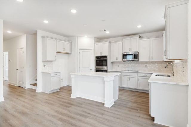 kitchen featuring light wood-type flooring, appliances with stainless steel finishes, decorative backsplash, and a sink