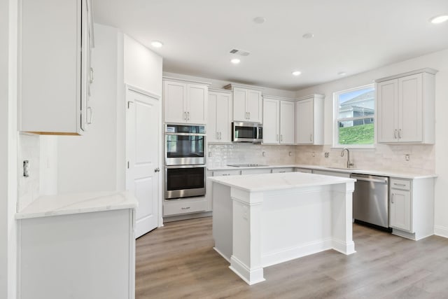 kitchen with stainless steel appliances, a sink, visible vents, backsplash, and light wood finished floors