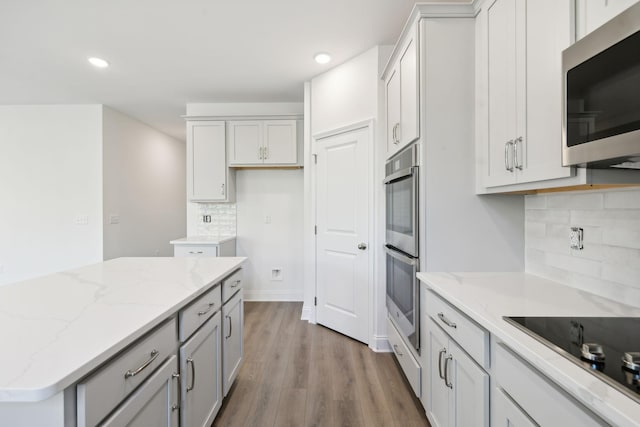 kitchen with stainless steel appliances, recessed lighting, wood finished floors, decorative backsplash, and light stone countertops