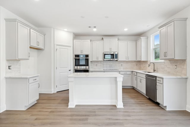 kitchen with stainless steel appliances, a kitchen island, a sink, light countertops, and light wood finished floors