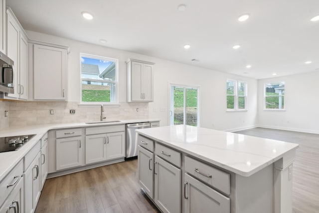 kitchen featuring light wood finished floors, black electric stovetop, gray cabinets, stainless steel dishwasher, and a sink