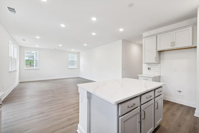 kitchen featuring a center island, tasteful backsplash, light stone countertops, gray cabinetry, and wood finished floors