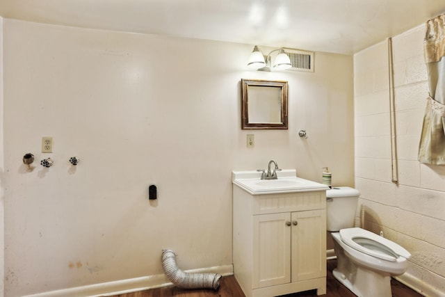 half bathroom featuring concrete block wall, toilet, and vanity