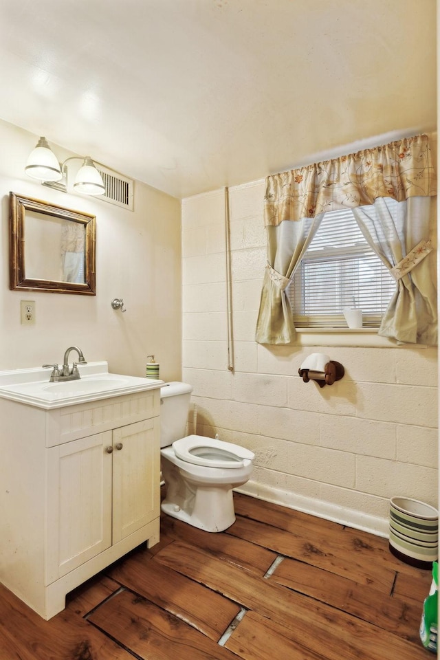 bathroom with vanity, concrete block wall, toilet, and wood finished floors