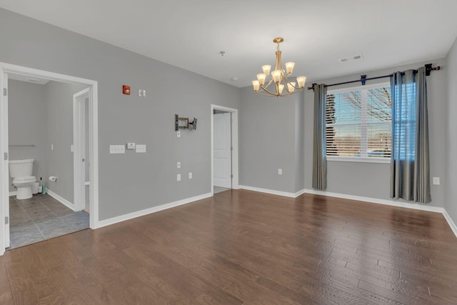 empty room with an inviting chandelier, baseboards, visible vents, and wood finished floors