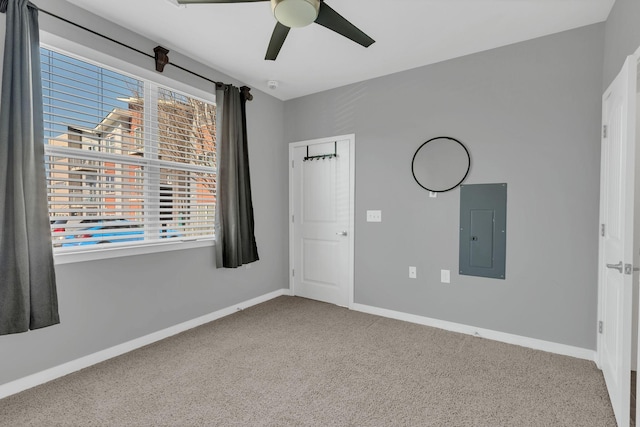 unfurnished bedroom with carpet floors, a ceiling fan, electric panel, and baseboards