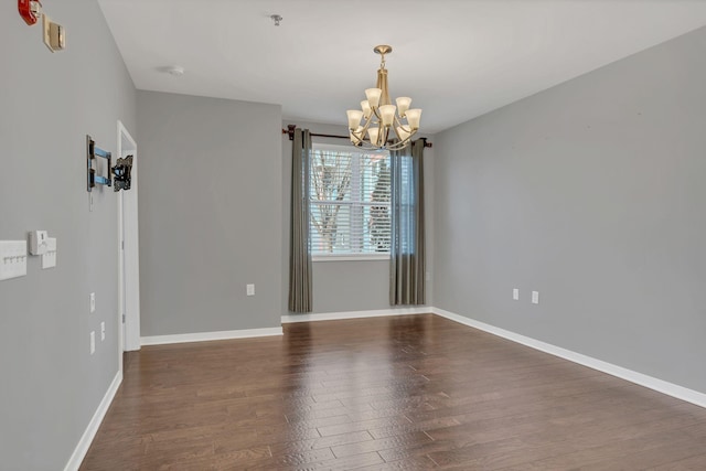 unfurnished room featuring a notable chandelier, baseboards, and wood finished floors