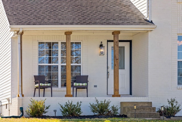 doorway to property with brick siding, a porch, and a shingled roof