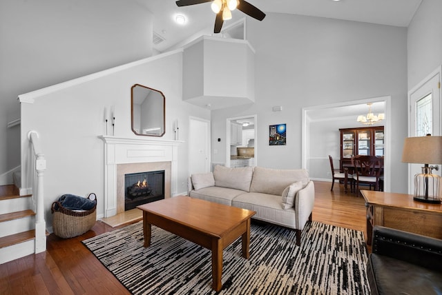 living area with high vaulted ceiling, ceiling fan with notable chandelier, a premium fireplace, stairs, and wood-type flooring