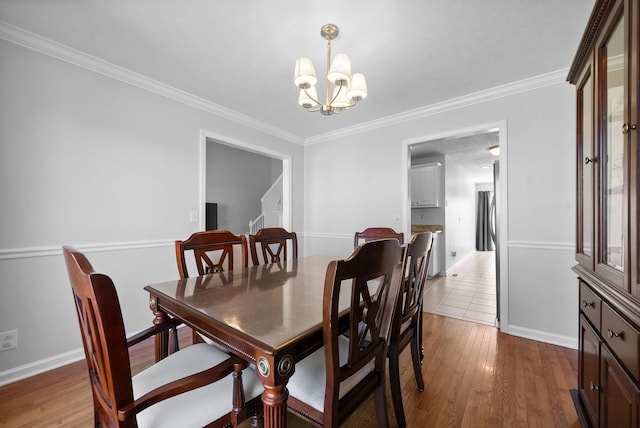 dining room featuring light wood-type flooring, crown molding, baseboards, and a notable chandelier