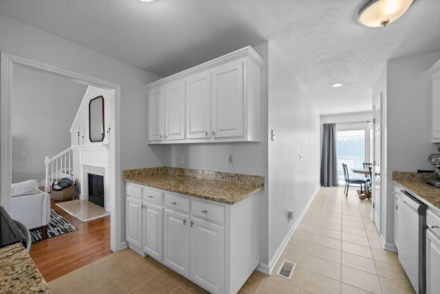 kitchen featuring light tile patterned floors, visible vents, white cabinets, dishwasher, and a textured ceiling