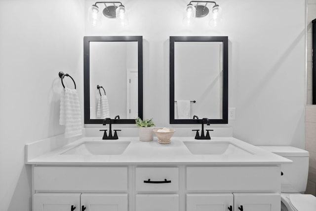 bathroom with a sink, toilet, and double vanity