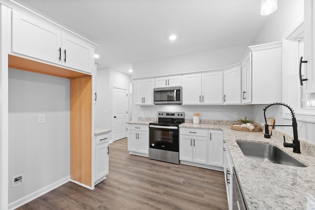 kitchen featuring light stone counters, stainless steel appliances, white cabinetry, a sink, and wood finished floors