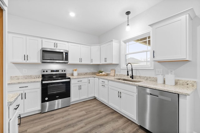 kitchen featuring stainless steel appliances, a sink, white cabinetry, light wood-style floors, and hanging light fixtures