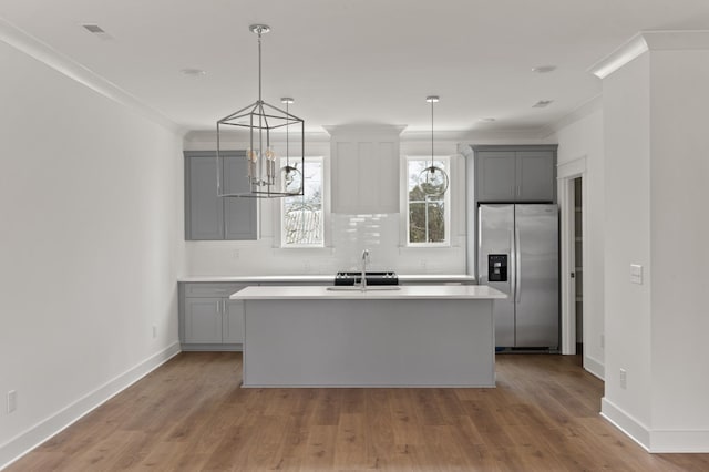 kitchen with a sink, gray cabinets, stainless steel fridge, and a kitchen island with sink