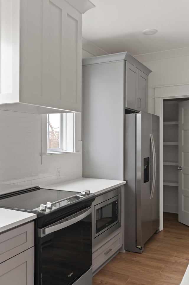 kitchen with stainless steel appliances, tasteful backsplash, light countertops, gray cabinetry, and light wood-style floors