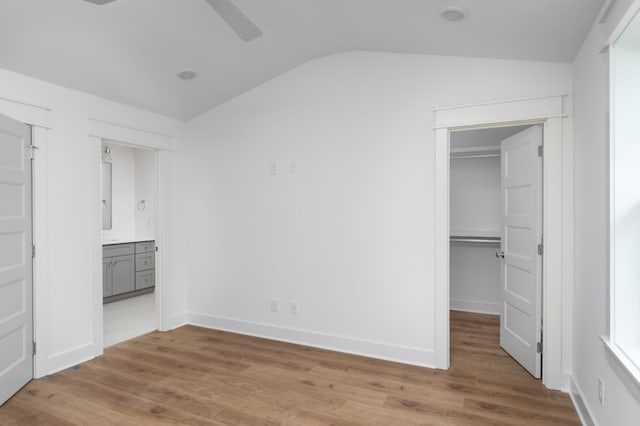 unfurnished bedroom featuring lofted ceiling, wood finished floors, a walk in closet, and baseboards