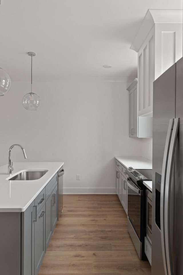 kitchen with light countertops, light wood-style flooring, gray cabinetry, appliances with stainless steel finishes, and a sink