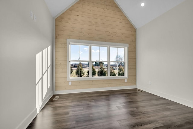 empty room featuring baseboards, wooden walls, high vaulted ceiling, and dark wood-type flooring