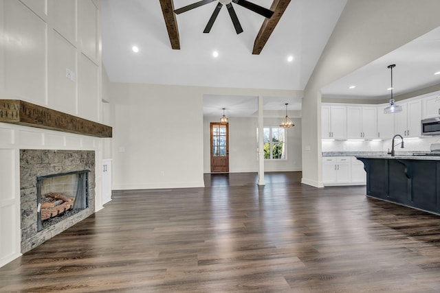 unfurnished living room with baseboards, dark wood-type flooring, a stone fireplace, a sink, and ceiling fan with notable chandelier