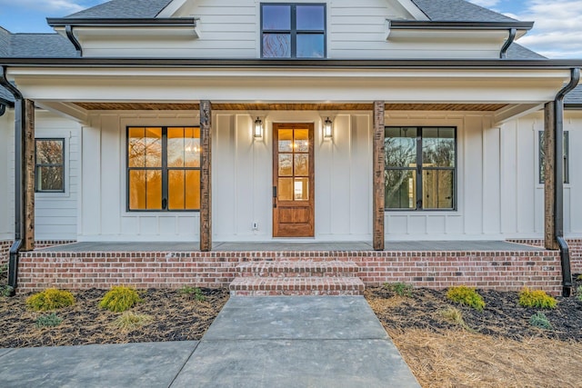 entrance to property with covered porch, roof with shingles, and board and batten siding