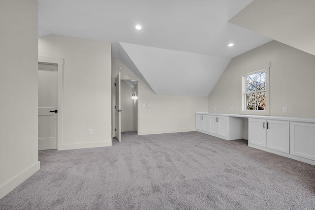 bonus room featuring lofted ceiling, light carpet, built in desk, and baseboards