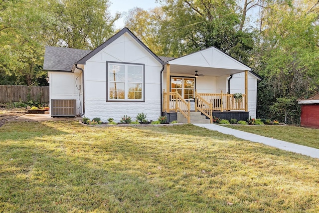 view of front of home featuring stone siding, roof with shingles, fence, cooling unit, and a front lawn