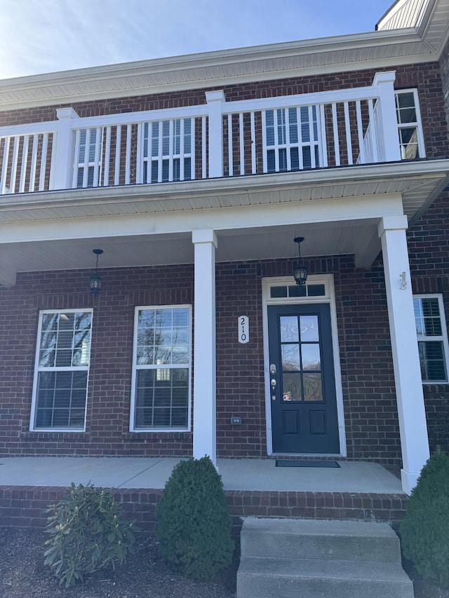 property entrance with covered porch, brick siding, and a balcony