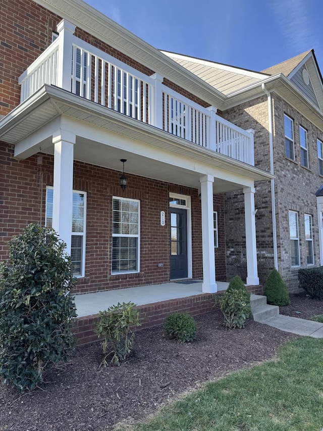 view of front of house with a porch, brick siding, and a balcony