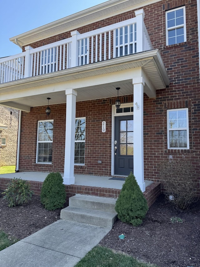 view of exterior entry with brick siding and a balcony