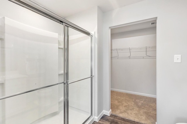 full bath featuring a walk in closet, a shower stall, and baseboards