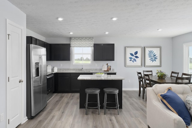 kitchen featuring stainless steel fridge, a breakfast bar area, light stone counters, dark cabinets, and a center island