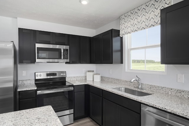 kitchen featuring dark cabinets, a textured ceiling, appliances with stainless steel finishes, and a sink