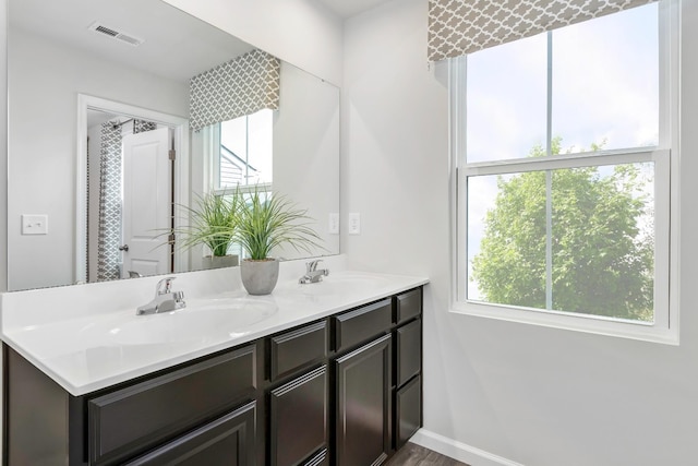 bathroom with double vanity, a sink, visible vents, and baseboards